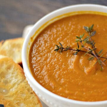 A bowl of carrot ginger soup topped with fresh thyme sprigs, with crostini on the side.