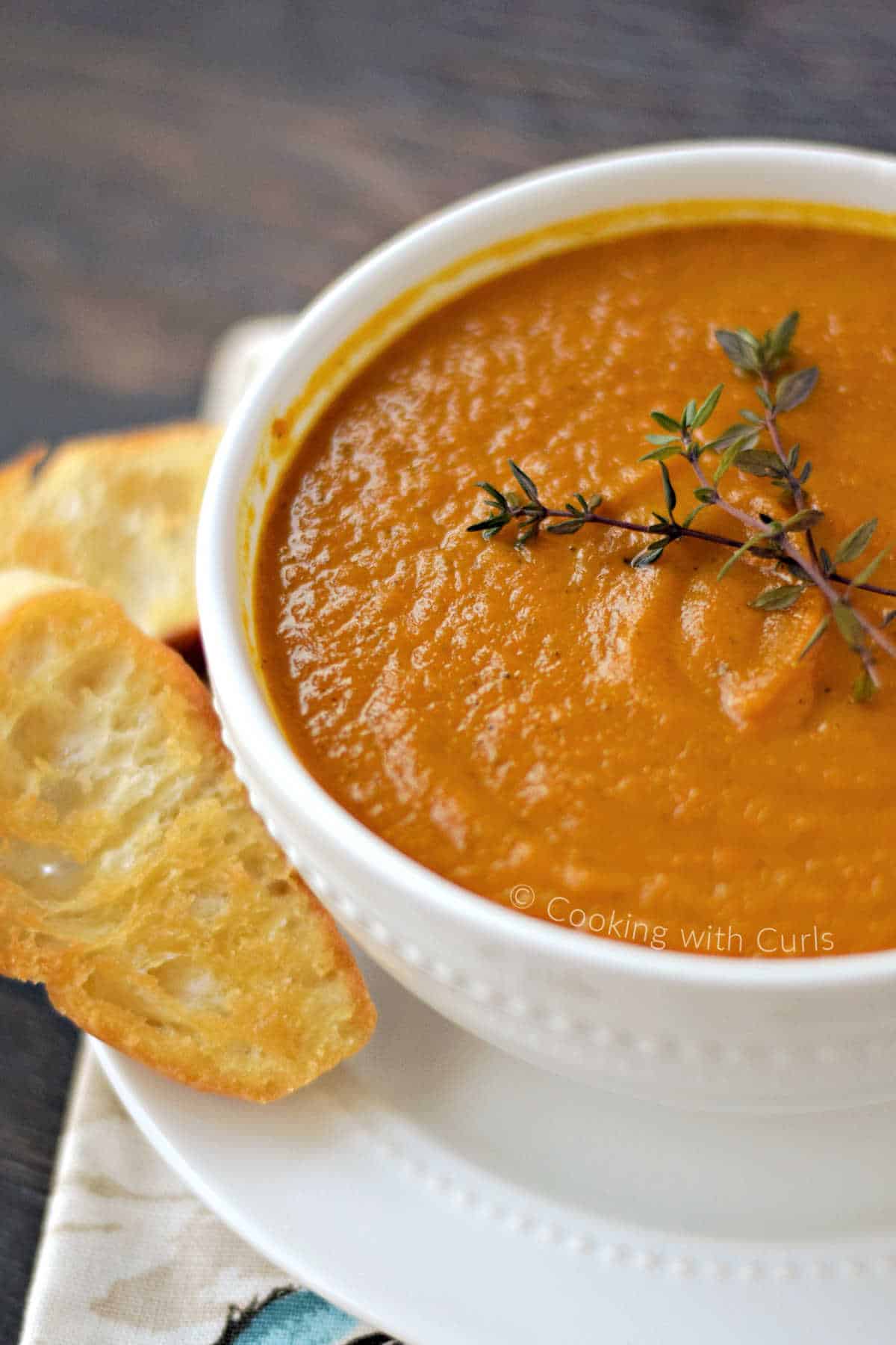 A bowl of carrot ginger soup topped with fresh thyme sprigs, with crostini on the side.