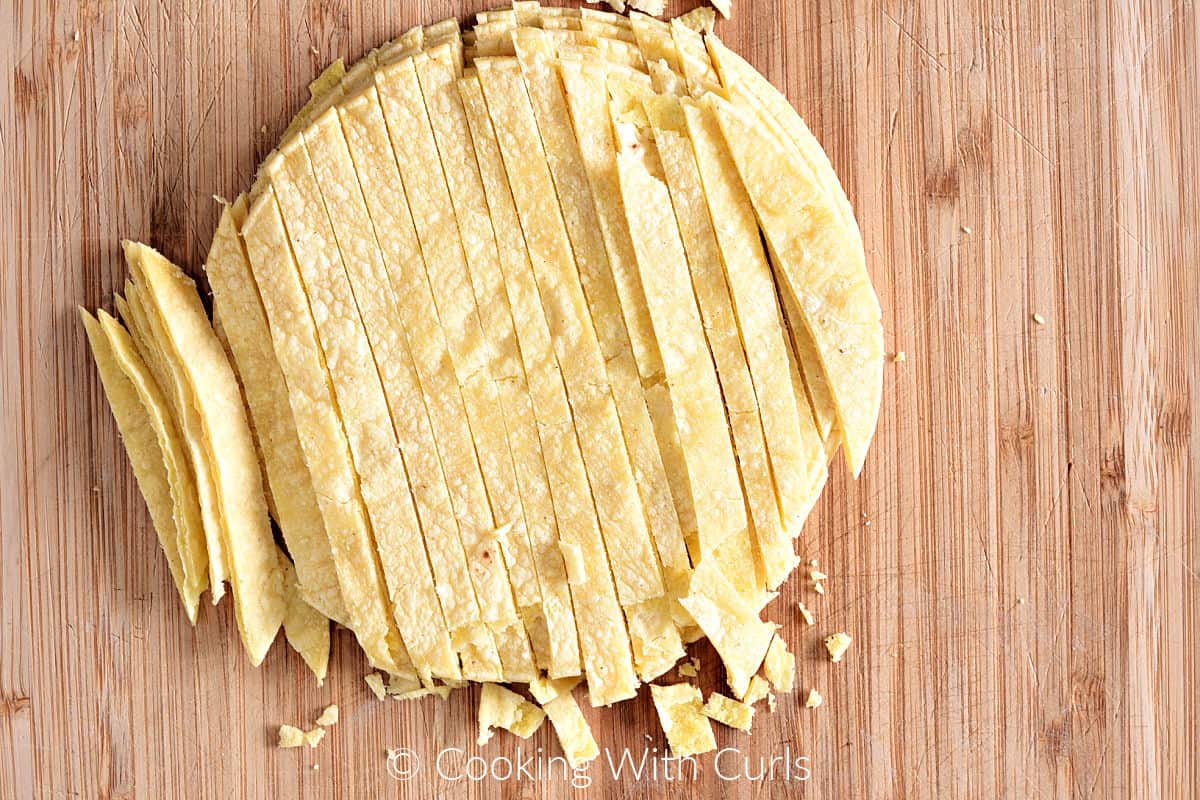 A stack of corn tortillas cut into thin strips on a wood cutting board.