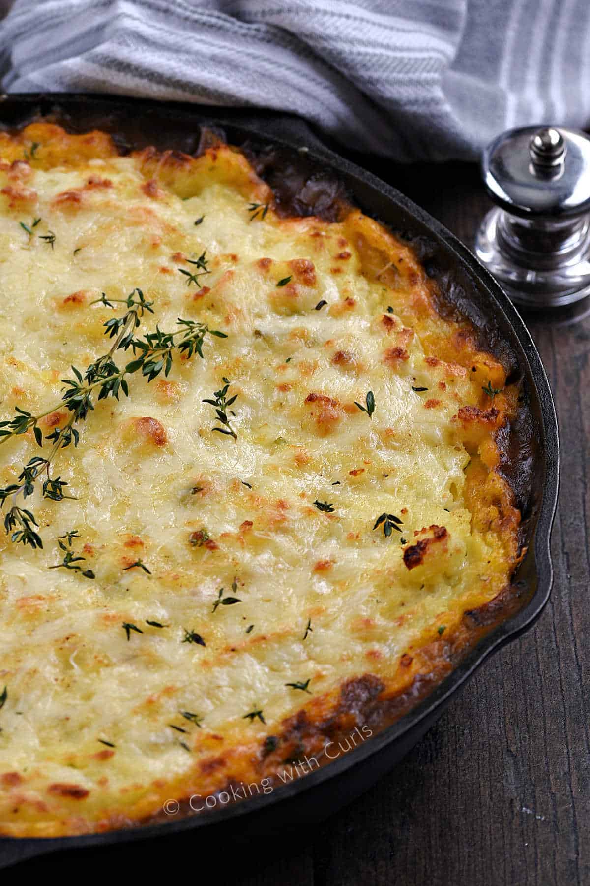 Bubbly classic Cottage Pie topped with fresh thyme in a cast iron skillet. 