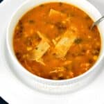 Chicken Tortilla Soup with beans, corn, tomatoes, chicken and cilantro served in a white bowl sitting on a large white plate