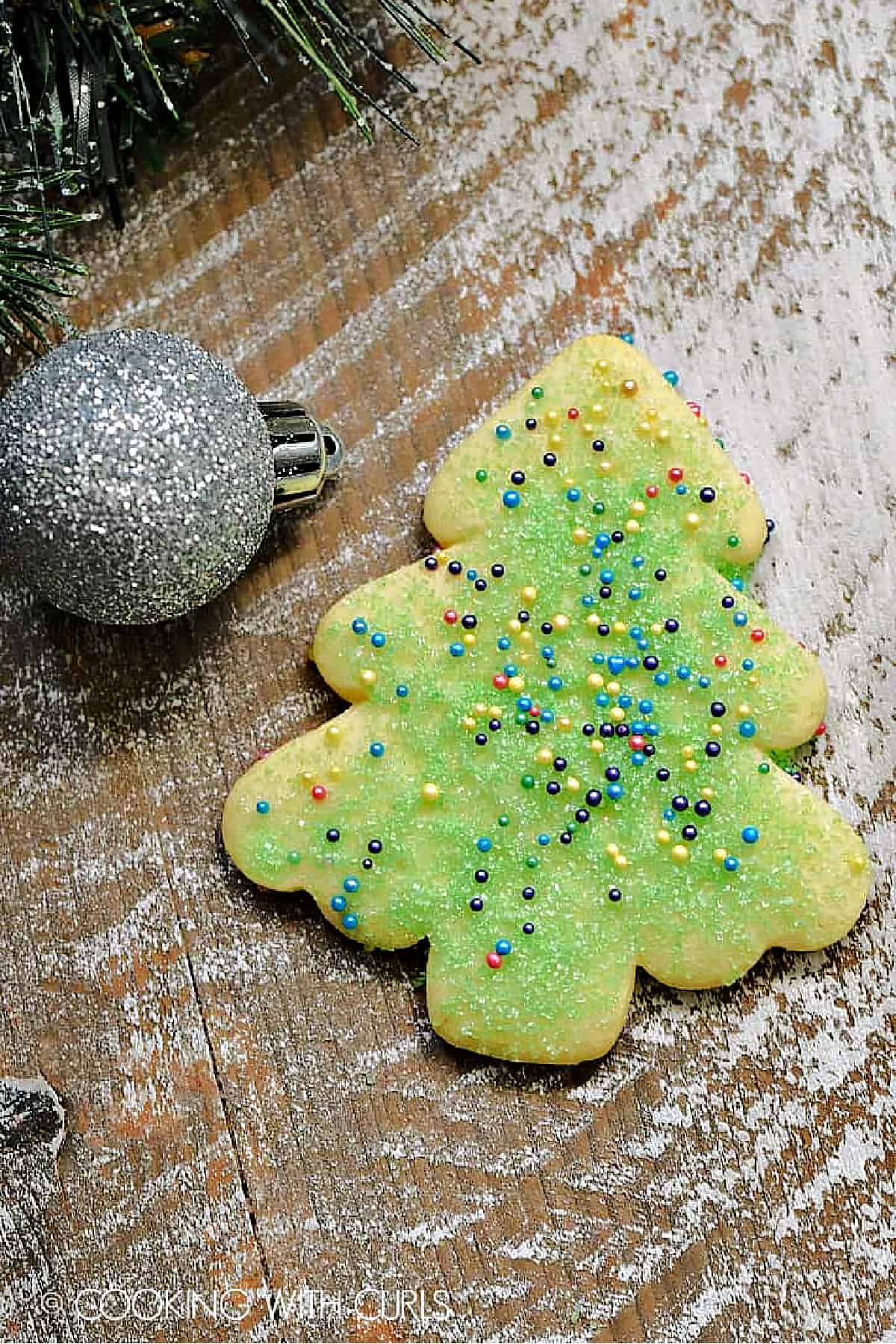 A cut-out sugar cookie tree decorated with green sugar and colored sprinkles.