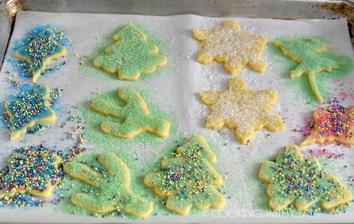 Twelve cookie cut-outs with sugar and sprinkles on a parchment paper lined baking sheet.