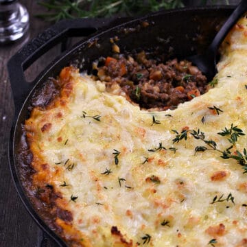 Cottage Pie topped with cheesy potatoes with a scoop of beef filling scooped out of a cast iron skillet.