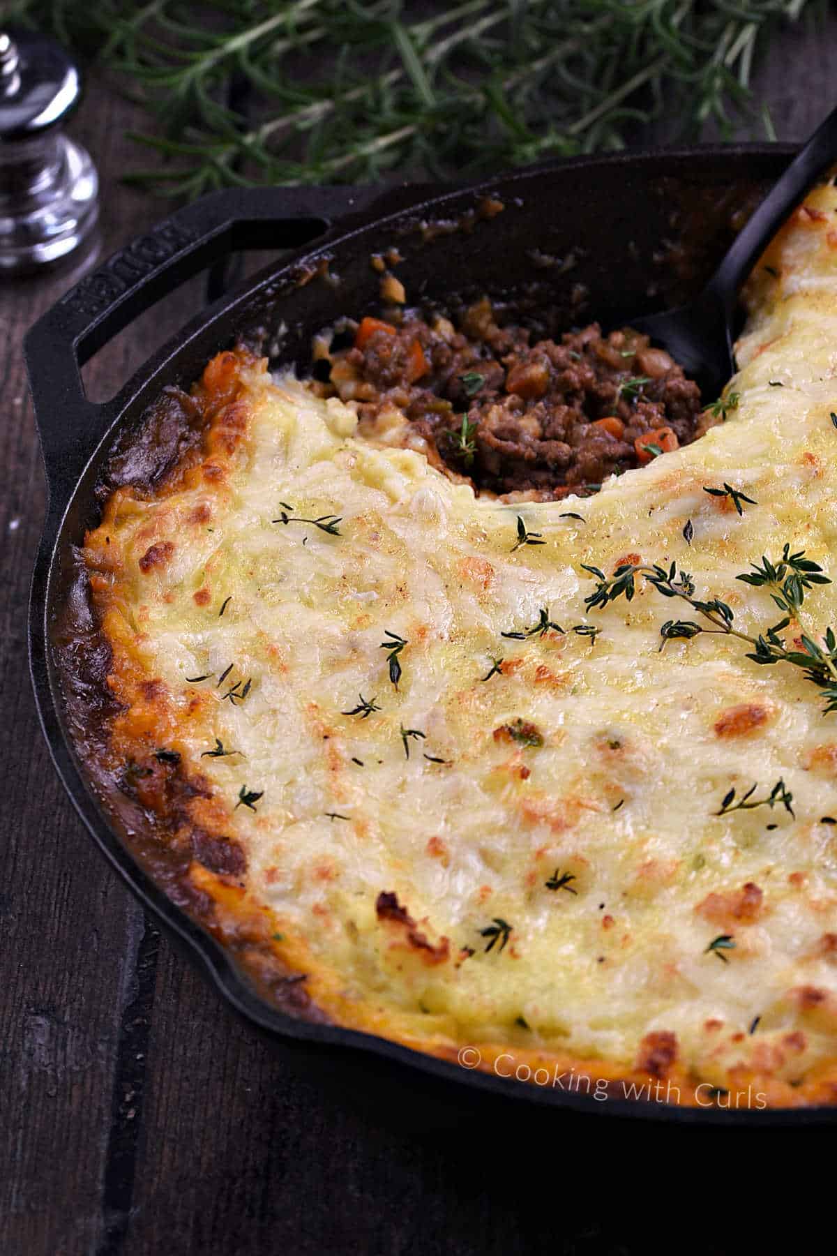 Cottage Pie topped with cheesy potatoes with a scoop of beef filling scooped out of a cast iron skillet. 