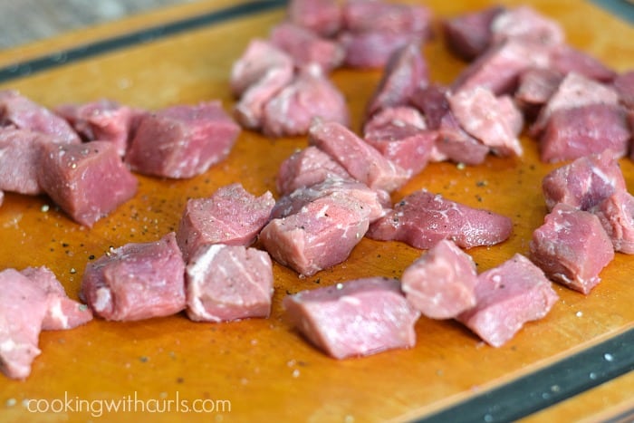 Chopped beef cubes on a cutting board topped with salt and pepper.