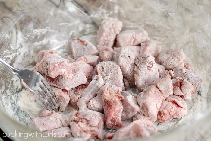 Beef cubes tossed with flour in a glass bowl.