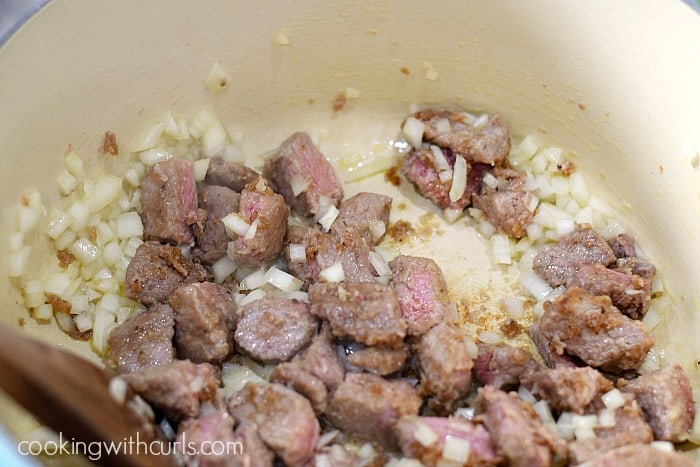 Browned steak with diced onions in a large pot.