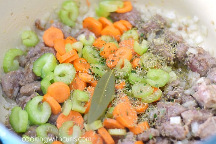 Celery and carrots slices with herbs and a bay leaf over the cooked steak and onions.