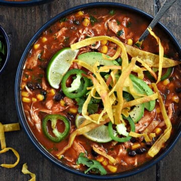 Looking down on a bowl of chicken tortilla soup recipe topped with sliced jalapenos, avocado slices, cilantro, and fried corn tortilla strips.
