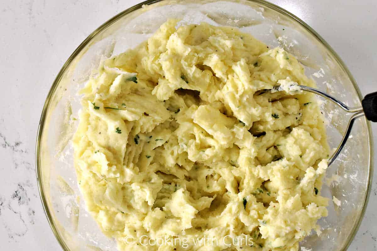 Mashed potatoes with chopped parsley and grated cheese in a large mixing bowl. 
