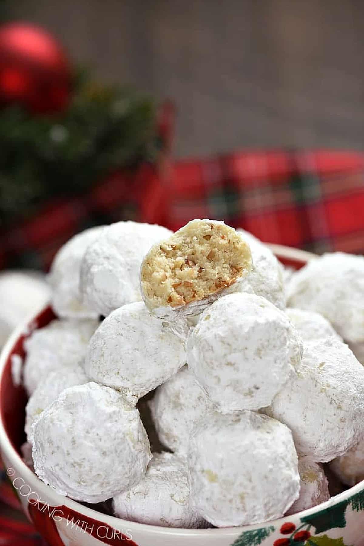 Pecan Snowballs stacked on top of each other in a holiday serving bowl surrounded by tartan plaid.
