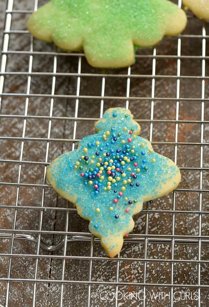 Two sugar cookies decorated with colored sugar and sprinkles on a wire rack.