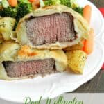 beef tenderloin wrapped in puff pastry served on a white plate with roast potatoes, broccoli and carrots