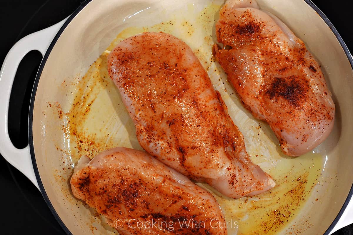 Three boneless skinless chicken breasts with taco seasoning in a large skillet. 