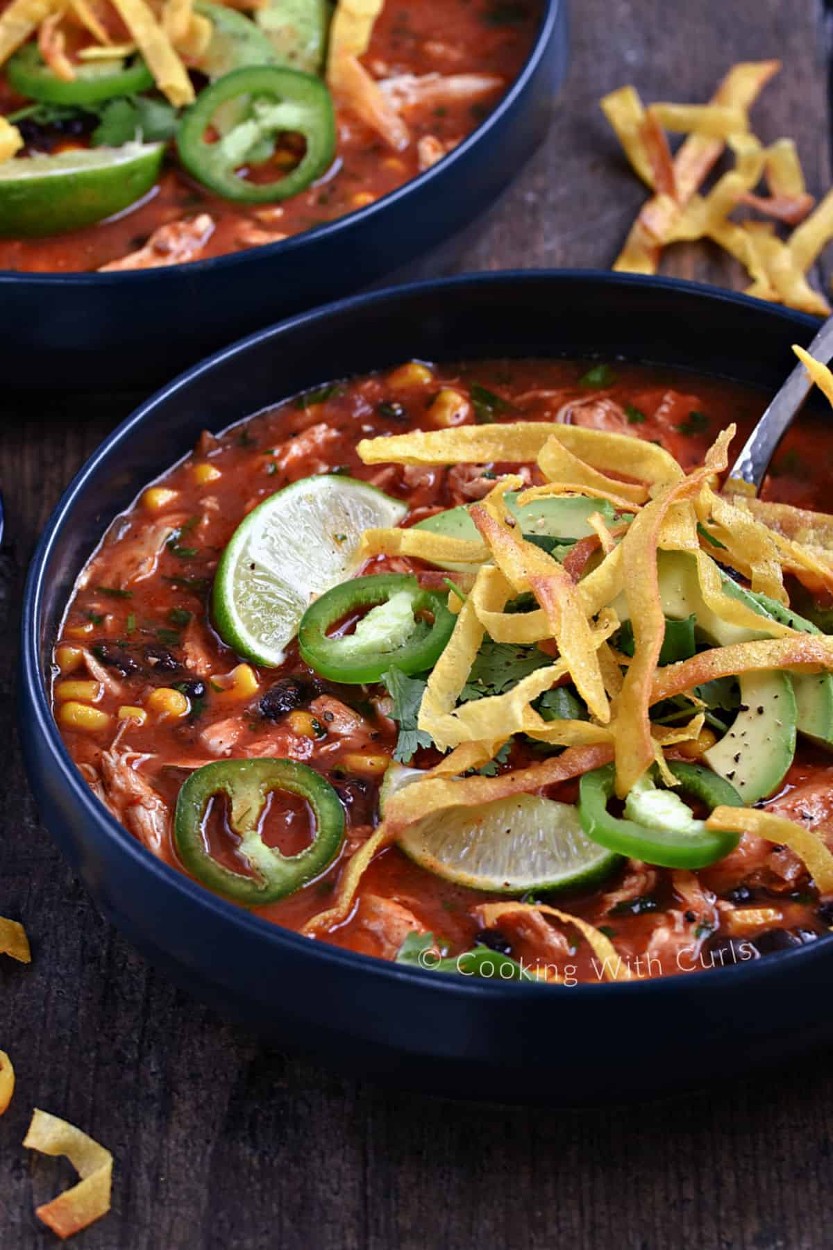 Two bowls of tomato, beans, and corn soup topped with sliced jalapenos and tortilla strips. 
