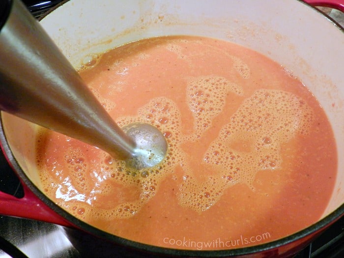 stick blender pureeing soup in a dutch oven on the stove