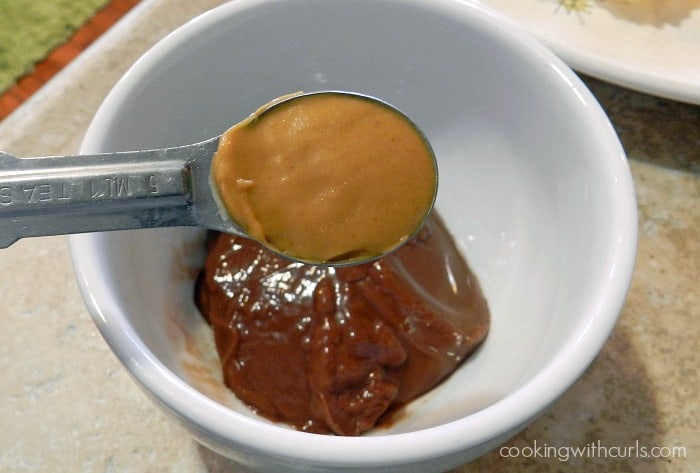 A small white bowl with a chocolate pudding cup inside with a teaspoon of peanut butter hovering over it. 