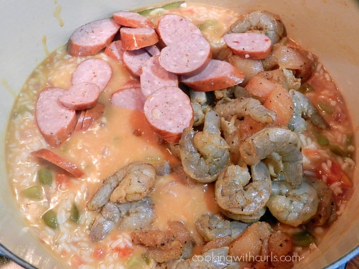 Sliced sausage, raw shrimp, and seasoned chicken pieces added to the rice mixture.