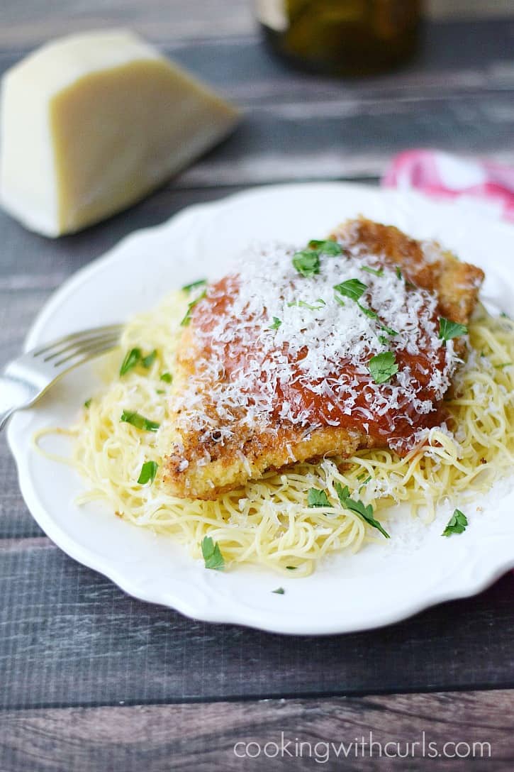 Chicken Parmesan served on a bed of of pasta topped with marinara sauce and grated parmesan cheese.