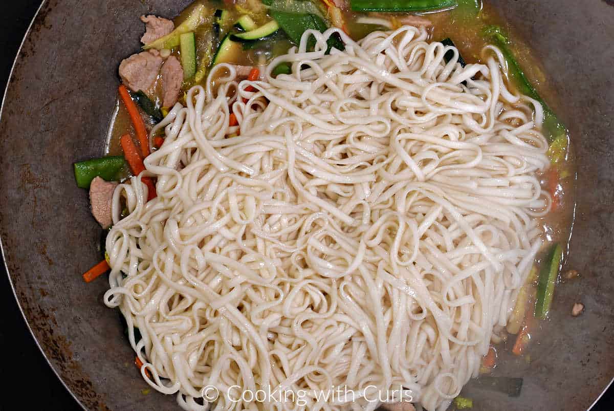 Cooked noodles on top of pork and vegetable stir fry in a wok. 