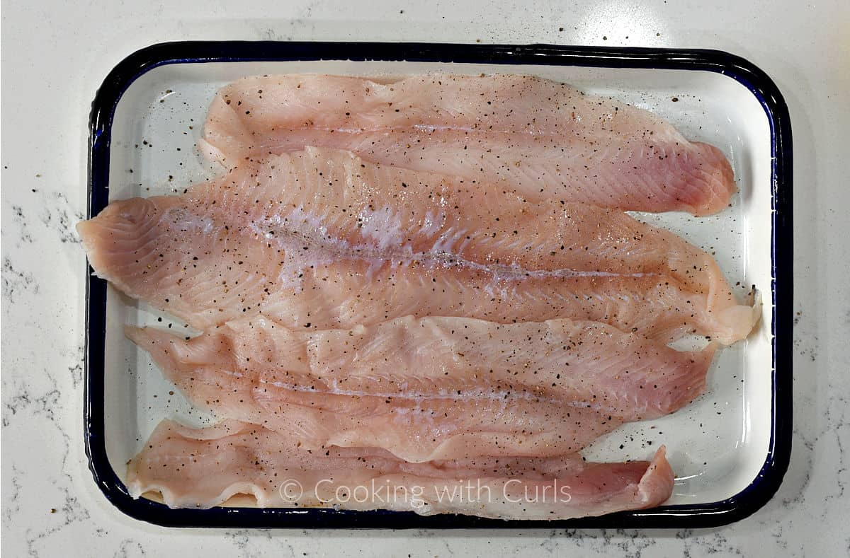 Four sole filets on a tray seasoned with salt and pepper. 