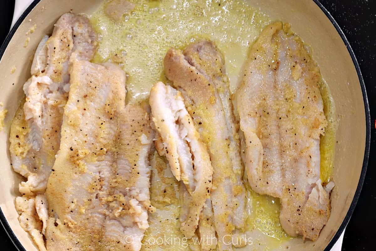 Four sole filets simmering in butter and oil in a large skillet. 