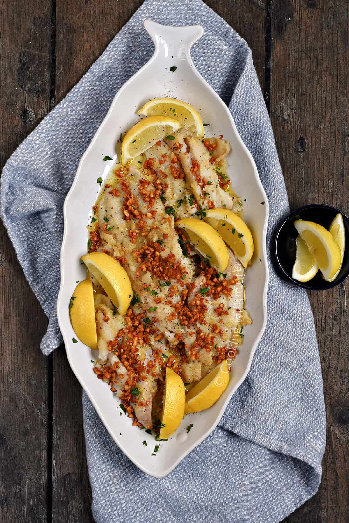 Looking down on a platter of sole covered with caramelized garlic and lemon wedges. 