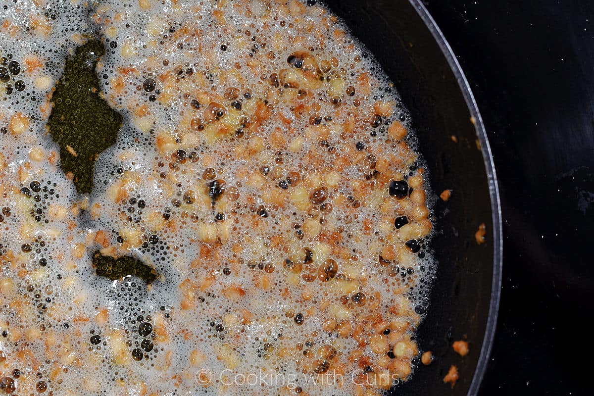 Minced garlic simmering in hot butter and oil in a skillet. 
