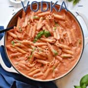 Penne pasta in a creamy tomato sauce topped with grated cheese and fresh basil in a white skillet.