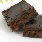 two dark fudgy avocado brownies leaning against each other on a white plate.