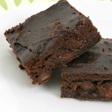 two dark fudgy avocado brownies leaning against each other on a white plate.