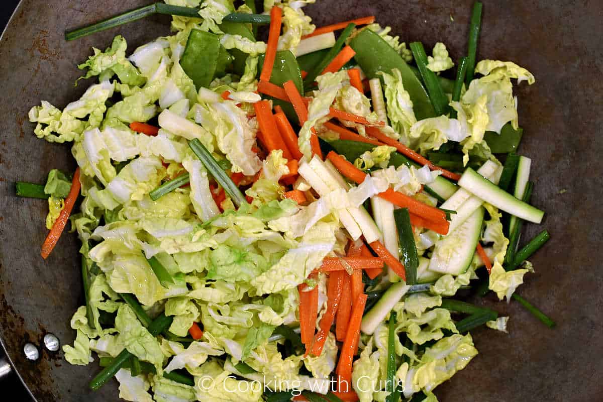 Strips of cabbage, carrots, zucchini, green onions, and snow peas in a wok. 