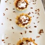 Five Mocha Pie Bites lined up on a rectangle white plate with chocolate shavings scattered around.