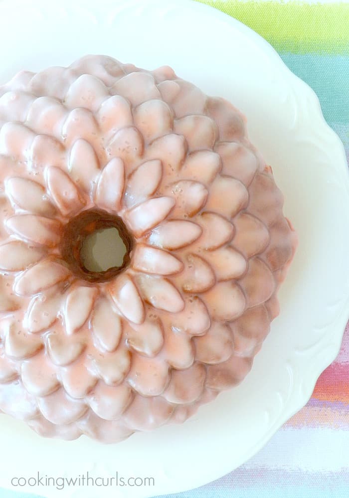 A pink bundt cake with a flower pattern covered in pink glaze and sitting on a large white plate.
