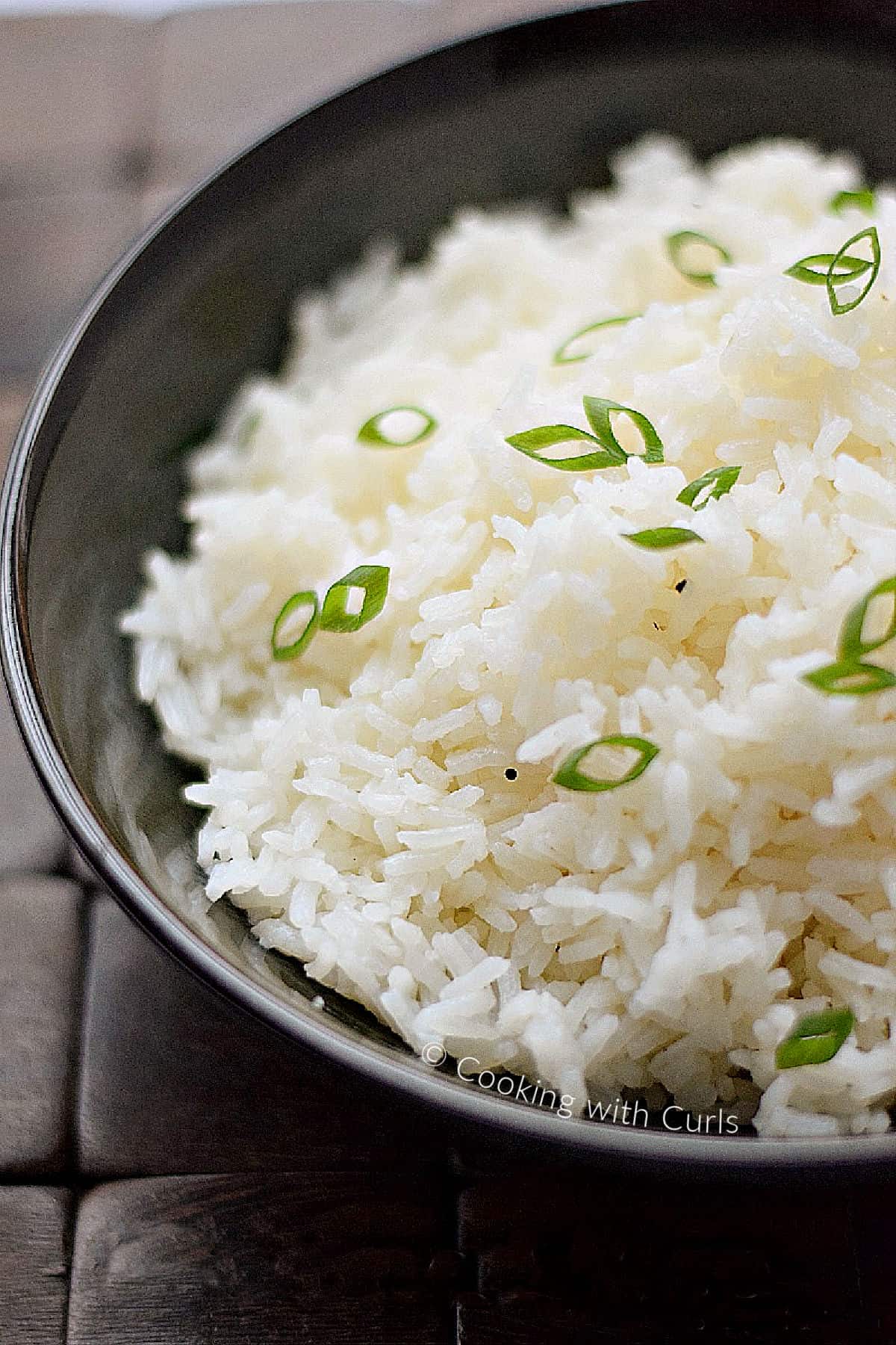 A bowl of steamed rice with black pepper and sliced green onion on top. 