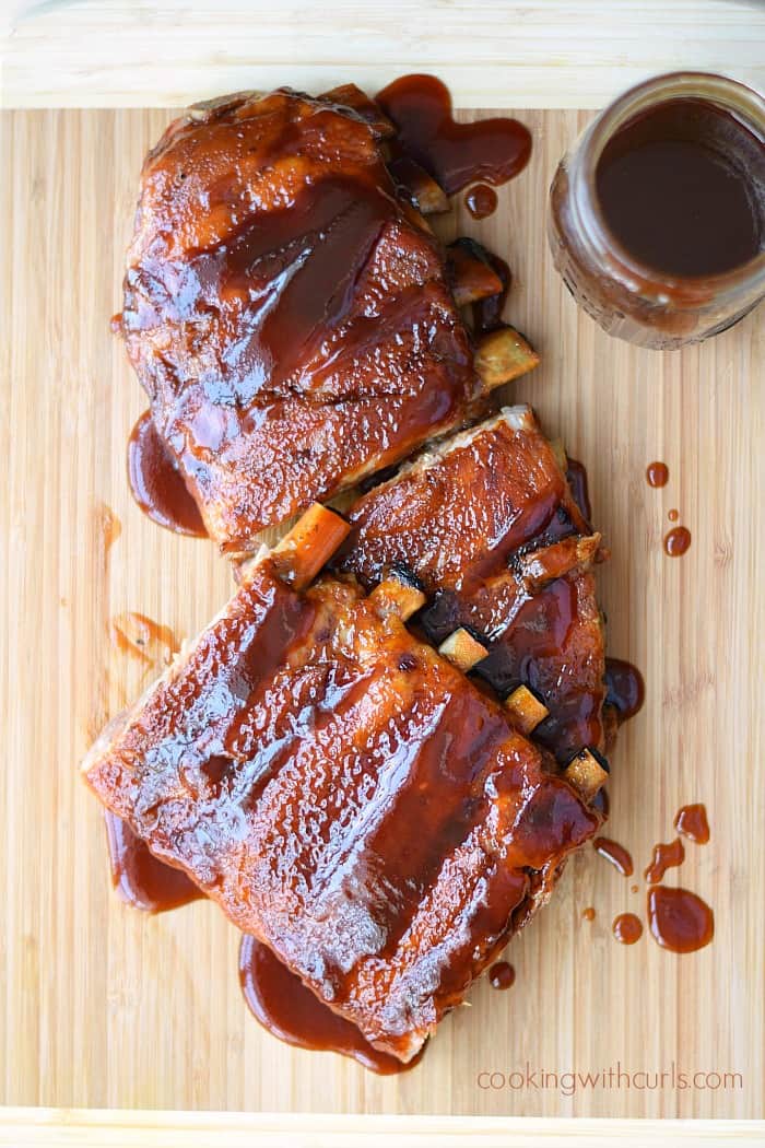 A slab of Guinness Barbecue Ribs on a wood cutting board with a jar of barbecue sauce in the upper right corner