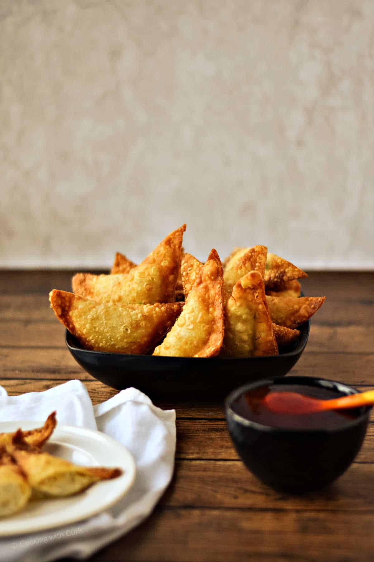 Crab rangoons in a serving bowl with a small bowl of sweet and sour sauce on the side.