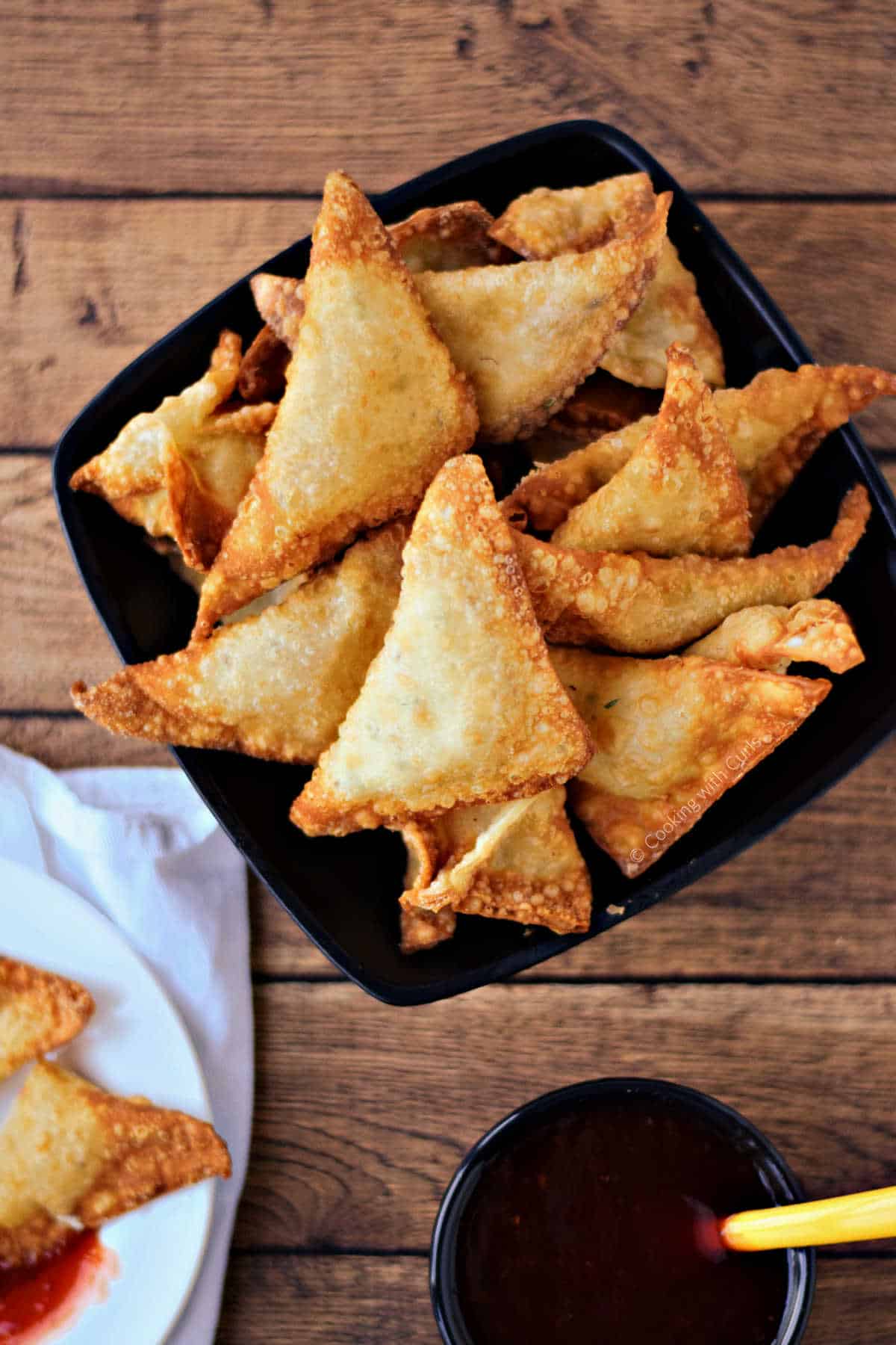Crab rangoons in a bowl with a small bowl of sweet and sour on the side.
