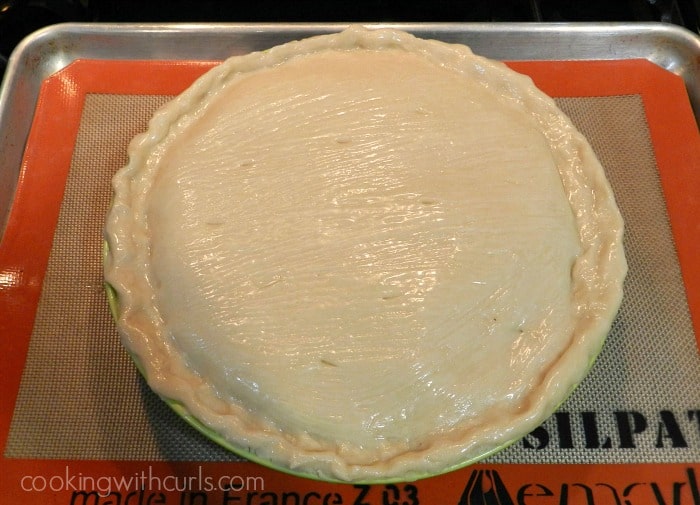 Filled lobster pot pie brushed with egg wash sitting on a silicone lined baking sheet. 