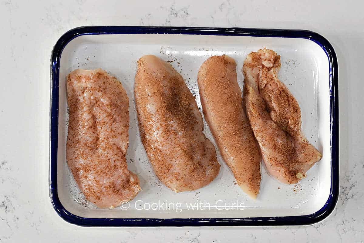Four seasoned chicken breasts on a tray.