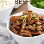 Sauce covered strips of beef garnished with green onions in a white cylinder style bowl with bowls of rice and broccoli in the background.