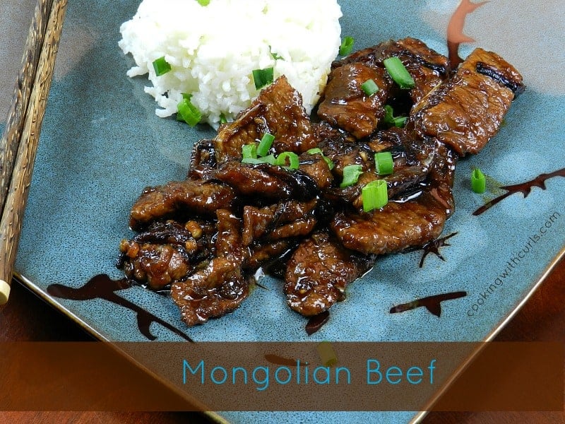 Sauce covered strips of beef on a blue plate with steamed rice and wooden chop sticks on the left side.