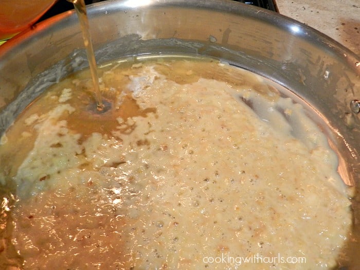 Seafood stock being poured into the roux in a large skillet. 