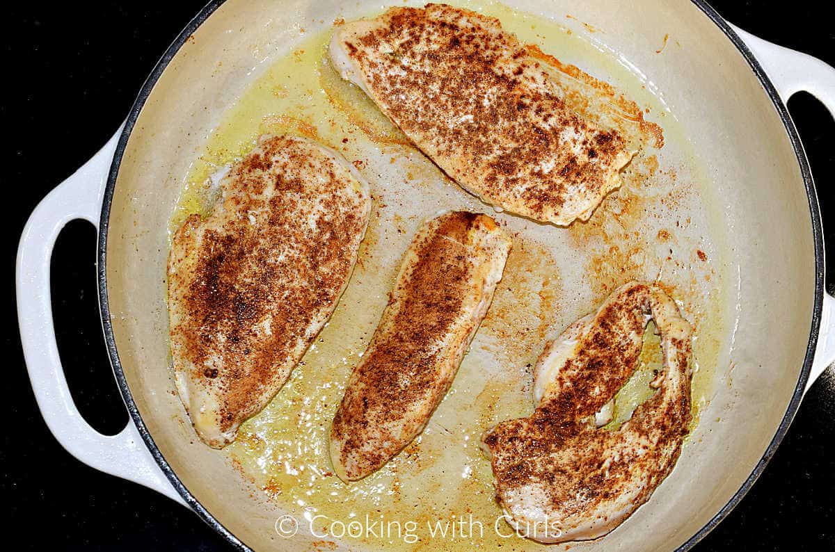 Four seasoned chicken breasts cooked in a cast iron skillet.