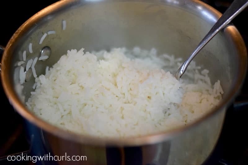 Fluffing cooked, white rice in a saucepan with a fork.