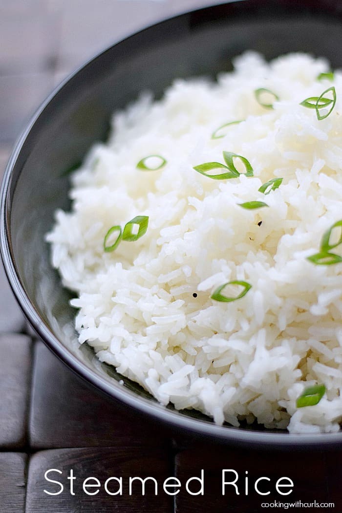 steamed rice in a black bowl sitting on a wooden placemat