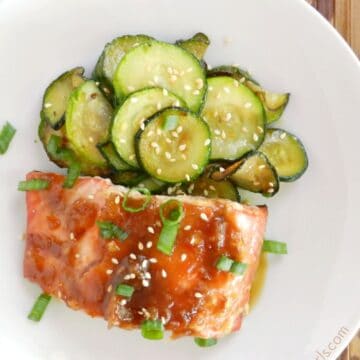 teriyaki sauce covered salmon on a white plate with sauteed zucchini rounds