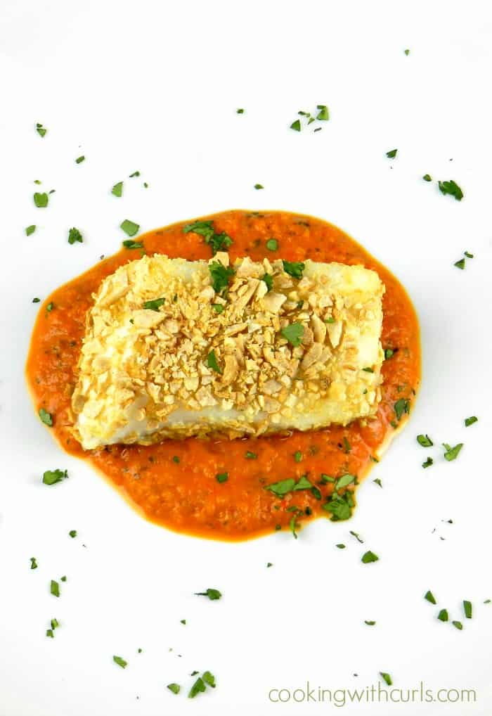 large white plate with roasted red pepper puree in the center with tortilla crusted sea bass laying on top and cilantro sprinkled over the entire plate