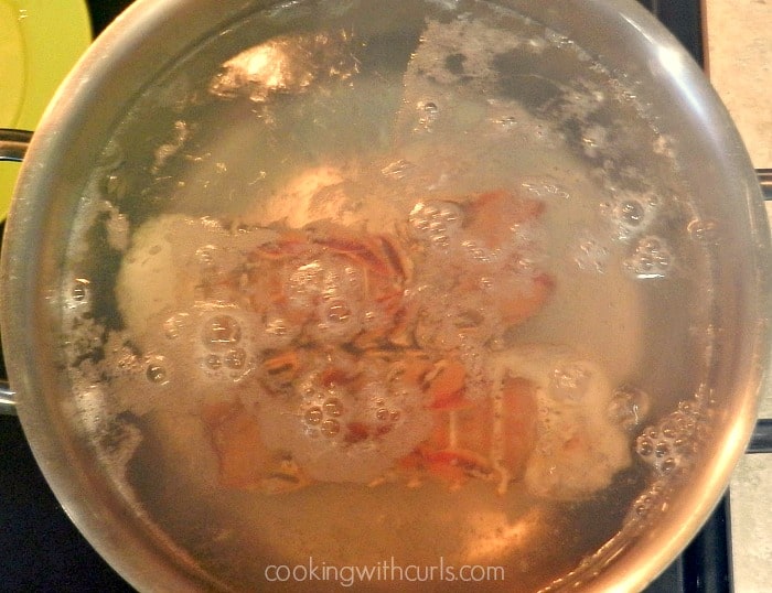 Two lobster tails boiling in water inside a large pot. 